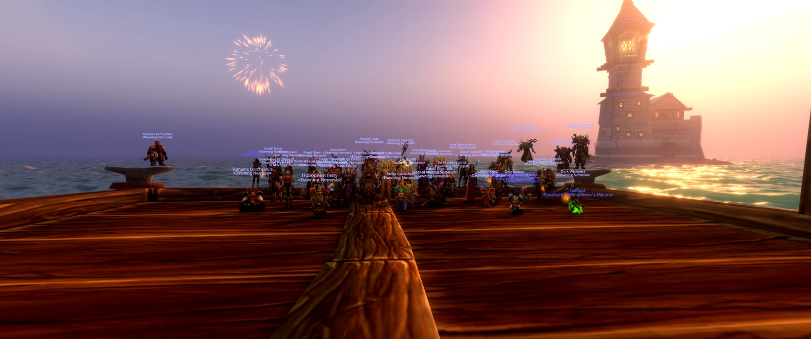 A firework bursts above Dawning Nemesis members posing on the dock beside the lighthouse at sunset.